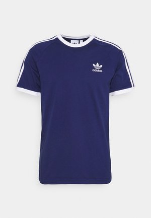 T-shirt en coton bleu marine avec des accents blancs, doté d'un col rond, de manches courtes et de trois rayures blanches sur chaque épaule. Petit logo sur la poitrine.