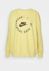 Žlutá mikina z bavlněné směsi, na přední straně s černým logem Nike a kruhovým textovým motivem, s žebrovanými manžetami a spodním lemem.