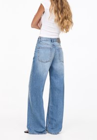 Jean large bleu clair en denim, avec une taille haute, un design à cinq poches et une texture délavée pour une coupe décontractée.