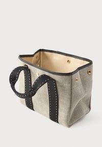 Μικρή μπεζ καμβά τσάντα χειρός με μαύρους διπλούς χερούλια και χρυσά κουμπιά, ανοιχτή κορυφή που δείχνει το άδειο εσωτερικό.