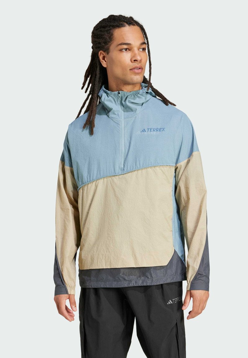Chaqueta ligera y multicolor con diseño de media cremallera, tejido texturizado y paneles en contraste en azul, beige y gris.