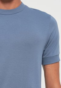 Short-sleeve, crew neck t-shirt in light blue cotton blend. Smooth texture with ribbed collar and cuffs, featuring a fitted design.