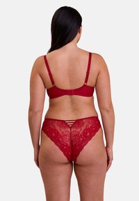 Ensemble de soutien-gorge et string en dentelle rouge avec de délicats motifs floraux, des bretelles ajustables et des détails en lacets sur le string. Texture douce.