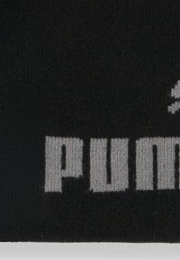 Tessuto a maglia nera con un logo grigio evidente e lettere testurizzate. Il design presenta una superficie liscia e un'estetica pulita e moderna.