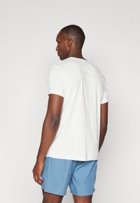 White short-sleeve t-shirt with a slightly textured back and a faint logo. Paired with light blue athletic shorts, showcasing a simple design.