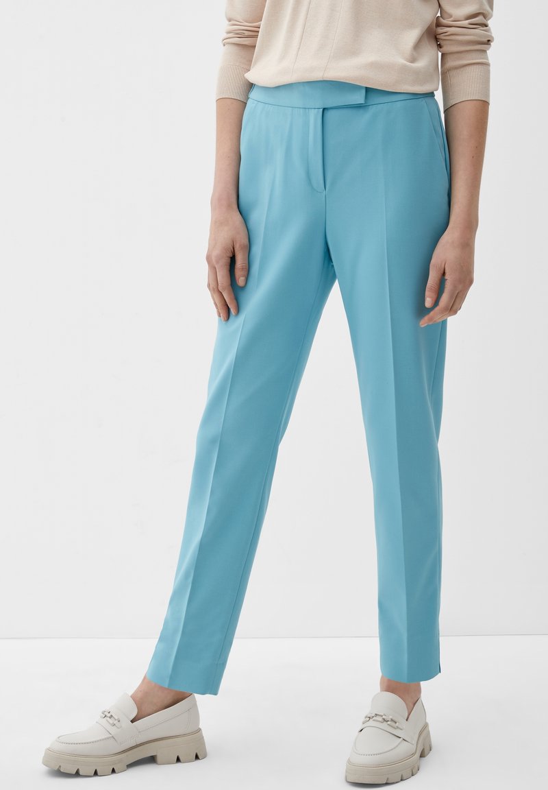 Pantalon bleu clair sur mesure avec une texture lisse et un devant plat. Associé à des mocassins blancs avec des semelles épaisses et des détails d'ornement discrets.