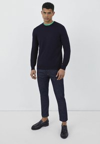 Maglione navy realizzato in materiale a maglia con colletto rotondo, abbinato a jeans scuri e mocassini neri. Il maglione ha maniche lunghe e un design semplice.