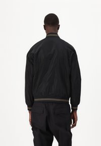 Black bomber jacket made from lightweight fabric, featuring ribbed cuffs and hem with gold accents, and a relaxed fit.