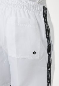 Pantalones cortos deportivos blancos con una cinta del logo negro de Nike a lo largo del costado, cintura elástica y un bolsillo de parche con un botón a presión negro.