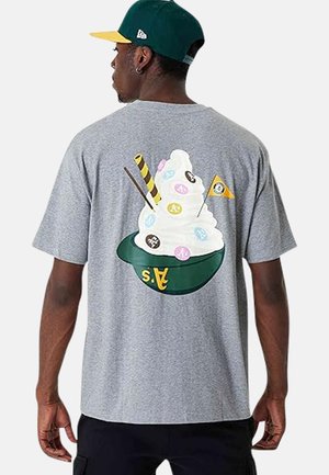 Mann trägt graues T-Shirt mit Grafik von Softeis in grüner Baseballkappe, verziert mit bunten Baseball-Logos und kleinem Fähnchen.