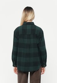 Roheline ja must ruuduline flanellsärk, millel on krae, nööpidega mansetid ja seljaosa detail. Pehme tekstuur, mugav lõige.