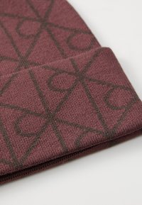 Maroon knit beanie with a geometric pattern in dark brown. Features a textured fabric and a folded cuff.