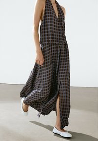 Sleeveless, check-patterned dress in dark brown and blue, featuring a gathered elastic waistband and side slits, paired with white flats.