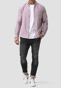 Lys rosa skjorte med knapper og en lomme, lagd over en hvid T-shirt med rund hals. Båret med mørke jeans og hvide sneakers.