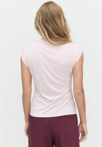 Vaaleanpunainen istuva paita, lyhyillä käännetyillä hihoilla, sileä pinta ja pyöreä kaula-aukko, yhdistettynä burgundinvärisiin housuihin.