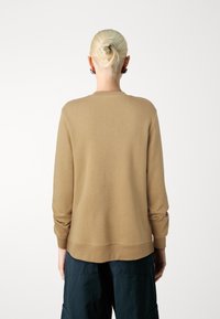 Sudadera de punto color beige con mangas largas, puños y dobladillo acanalados, con un escote redondo y una textura sutil. Colocada sobre un fondo liso.