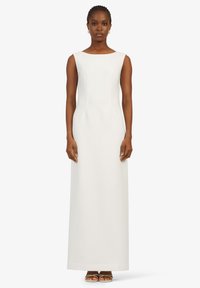 Robe blanche longue sans manches avec une coupe ajustée, décolleté carré et tissu lisse. Le tissu tombe droit jusqu'au sol.