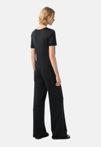 Zwarte, getailleerde T-shirt gecombineerd met wijde zwarte broek. De outfit heeft een zachte textuur en een elastische tailleband voor extra comfort.