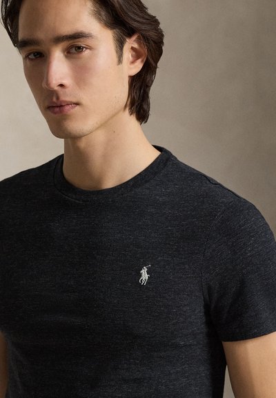 Svart t-skjorte med korte ermer laget av mykt stoff, med en liten hvit brodert logo på venstre bryst og rund hals.