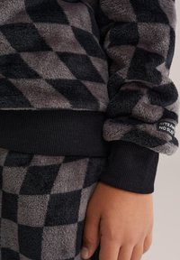Ropa de estar en casa de forro polar en un patrón de cuadros en negro y gris, con puños acanalados y una cinturilla. Textura suave y corte holgado.