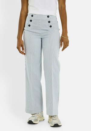 Pantalones de rayas finas azul claro de tiro alto con seis botones negros, llevados con camiseta blanca y zapatillas beige en una persona de pie.