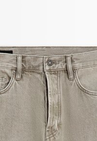 Lichtgrijze spijkerbroek met riemlussen, voorzakken en een metalen knoopsluiting aan de tailleband.