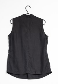 Černý bezrukávový top vyrobený z hladké tkaniny; má vysoký límec s zipem na zádech a zakřivený lem. Zavěšený na černém háčku.