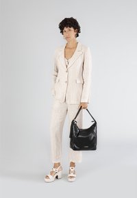 Blazer e pantaloni a righe beige chiaro, abbinati a sandali con piattaforma bianchi. Borsa nera con dettagli decorativi.