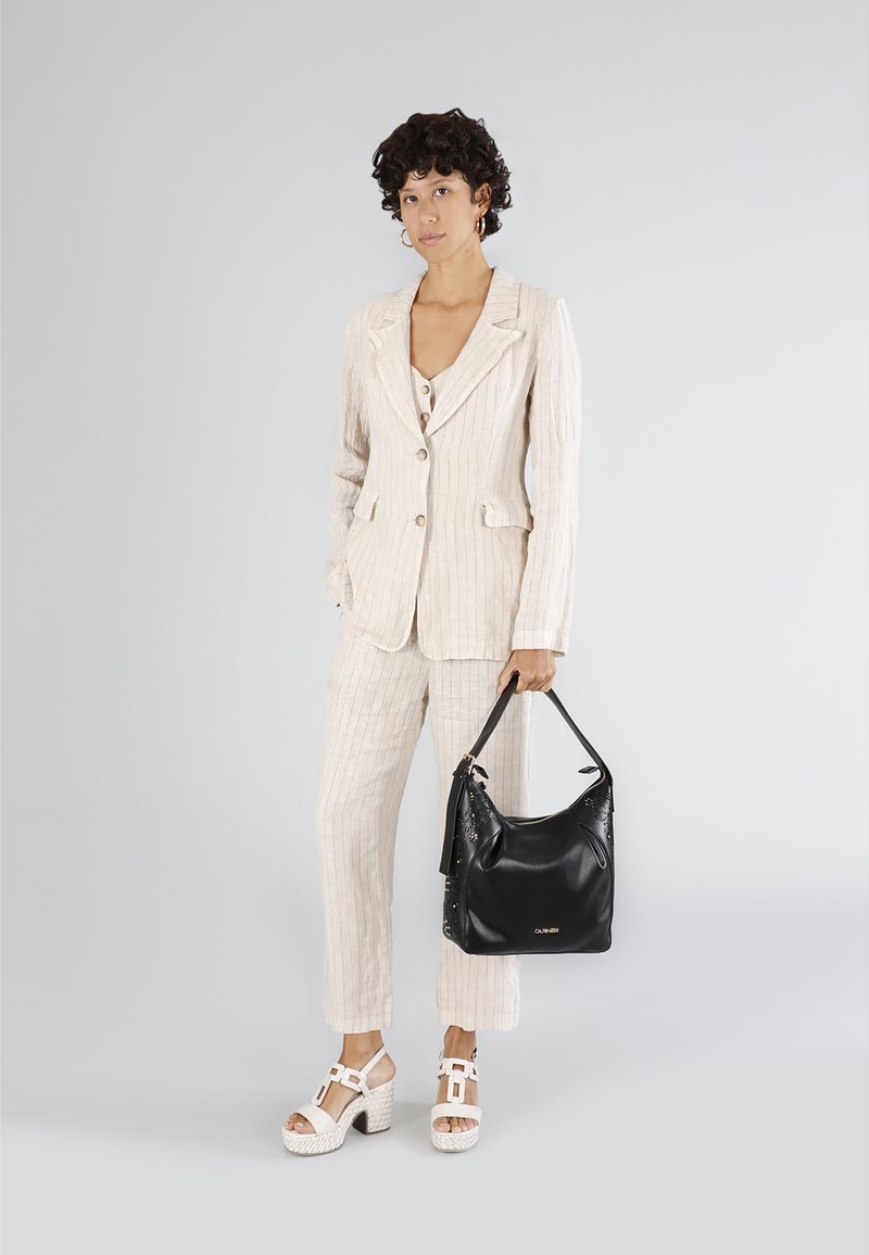 Blazer e pantaloni a righe beige chiaro, abbinati a sandali con piattaforma bianchi. Borsa nera con dettagli decorativi.