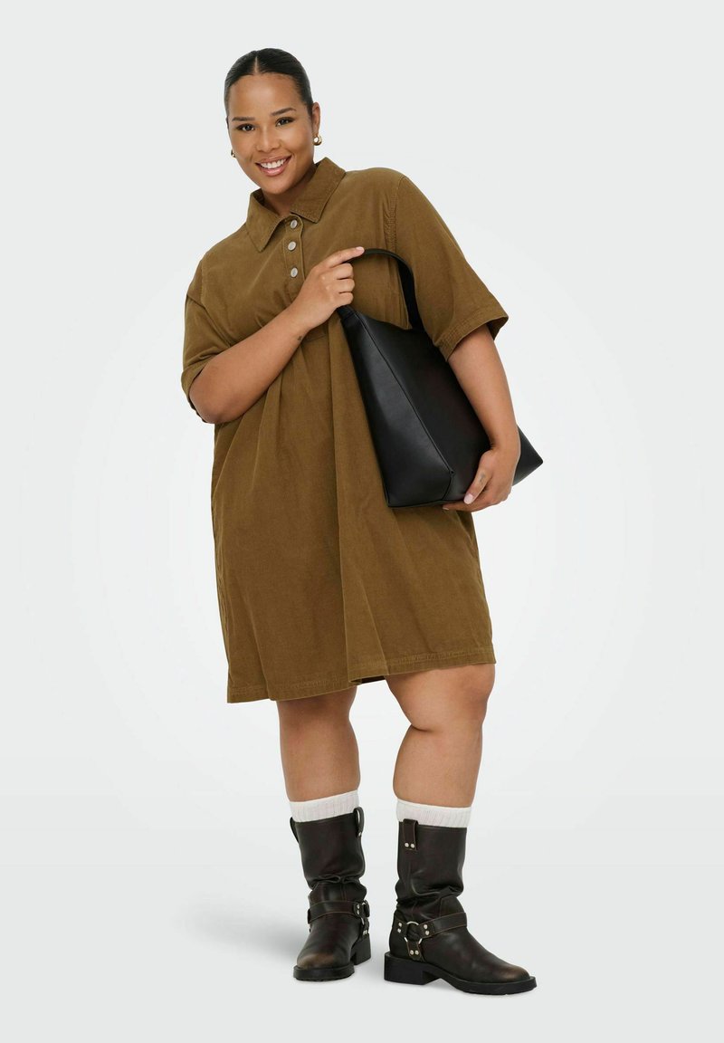 Robe chemise en velours côtelé marron avec un col, dotée de boutons et d'une coupe oversize. Associée à un tote en cuir noir et à des bottes marron montantes.