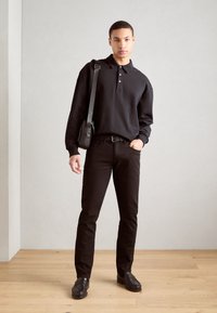 Camisa polo de manga larga negra con botones, combinada con jeans negros ajustados y mocasines negros. Se lleva un bolso bandolera negro sobre el hombro.