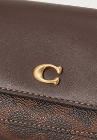 Rudas odinis piniginė su tekstūruota apdaila, ypatingai išsiskirianti auksine raide "C" ir kontrastingais siūlais.