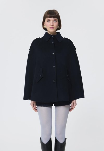 Cappa di lana blu navy con colletto alto, chiusura con bottoni e tasche frontali. Presenta una silhouette strutturata e dettagli sulle spalle.