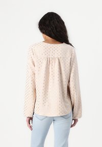 Blusa a maniche lunghe in tessuto rosa chiaro con un sottile motivo a pois dorati. Presenta un collo rotondo e un dettaglio arricciato sulla schiena per una vestibilità rilassata.