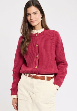 Cardigan rouge côtelé avec un col rond, des boutons en bois et des manches longues, associé à une jupe beige et une ceinture marron. Texture lisse.