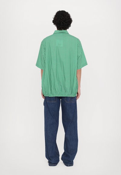 Green checkered short-sleeve shirt with a relaxed fit and elastic hem, paired with loose blue denim pants.