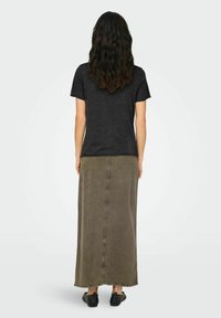 T-shirt nero a maniche corte abbinato a una lunga gonna di jeans verde oliva, con cucitura centrale e orlo sfrangiato, indossato con scarpe nere slip-on.