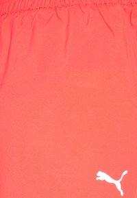 Pantalones cortos atléticos color coral con cintura elástica, textura suave y un logo blanco de Puma en la parte inferior izquierda.