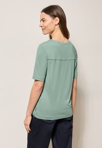 T-shirt verde chiaro a maniche corte con scollatura rotonda e un sottile dettaglio di cucitura sul retro, realizzato in tessuto morbido e traspirante.