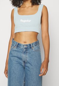 Jasnoniebieski krótki top z kwadratowym dekoltem, marszczonym dołem i białym logo "Pegador". W połączeniu z niebieskimi jeansami z wysokim stanem.