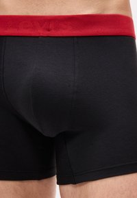 Gros plan sur un boxer noir avec une ceinture rouge arborant un subtil logo Levi's, porté par une personne.
