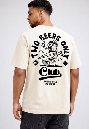 Mann trägt cremefarbenes T-Shirt mit schwarzer Grafik einer Cartoon-Bierdose, die ein Surfbrett hält, und dem Text "Two Beers Only Club, There Will Be More."