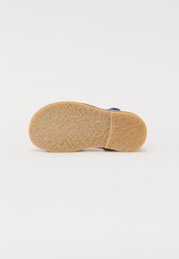 Sandal azul com material superior texturizado, sola de borracha castanha com uma superfície padronizada, apresentando detalhes de desgaste visíveis e design da sola.