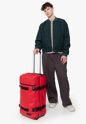 Red wheeled duffle bag with black straps, zippers, and accents. Rectangular shape, durable fabric, and retractable handle for easy transport.
