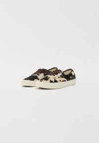 Cow-print canvas sneakers featuring brown laces, a white rubber sole, and a textured fabric, presented in a side view on a white background.