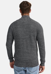 Suéter gris de manga larga con una tela texturizada, que presenta un cuello alto y puños ajustados, combinado con jeans de color azul claro. Vista posterior.