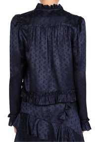 Navy zijden blouse met rimpel-kraag en manchet. Kenmerkend zijn het subtiele paisleypatroon, de geplooide achterkant en de gelaagde ruffles aan de zoom.