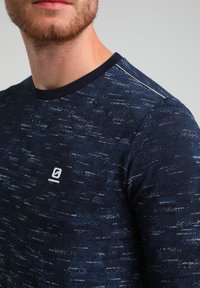 Camisa de manga larga azul marino con un patrón texturizado, que presenta un escote redondo y un pequeño logo en el pecho.