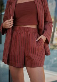 Ensemble bicolore de couleur rouille fabriqué dans un tissu léger, comprenant un haut sans manches et un short à taille élastique avec des rayures verticales.