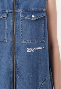 Denimu bez piedurknēm jaka ar priekšējo rāvējslēdzēju, divām krūšu kabatām un baltu izšūtu "KARL LAGERFELD JEANS" logo. Zila krāsa, teksturēta auduma.